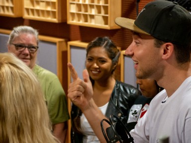 Rapper Kenny Anders staat in de opnamestudio met cursisten van de Bibliotheek West-Brabant. Hij telt af tot de cursisten mogen beginnen met zingen.