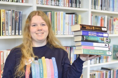 Een vrouwelijke bibliotheekmedewerker houdt een stapel boeken vast.